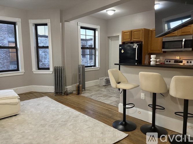 A kitchen with a black fridge, white chairs and a white rug.