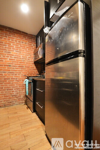 A kitchen with a black refrigerator and wooden floors.