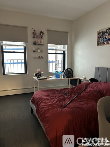 A bedroom with a red bedspread and a white desk with a lamp and a chair.