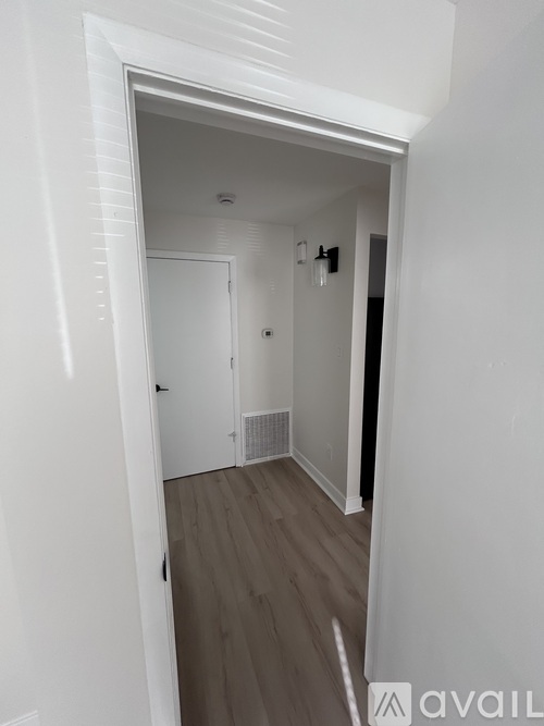A white hallway with a door and a wall-mounted light fixture.