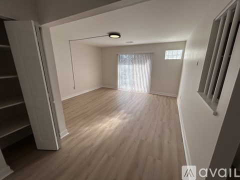 A spacious room with wooden flooring and a window with blinds.