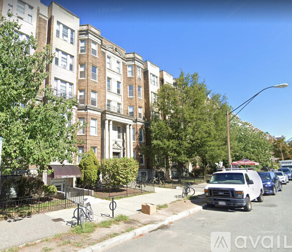 A street view of a residential area with apartment buildings, parked cars, and bicycles.