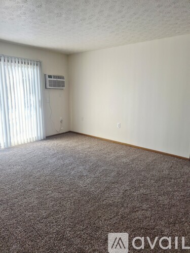 A carpeted room with a window and an air conditioner unit on the wall.