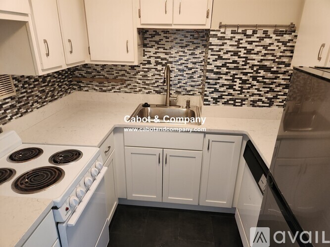 A kitchen with white cabinets and a black and white tiled backsplash.