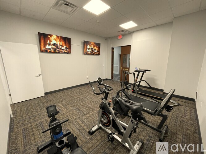 A gym room with exercise equipment and a wall-mounted TV showing a fireplace.