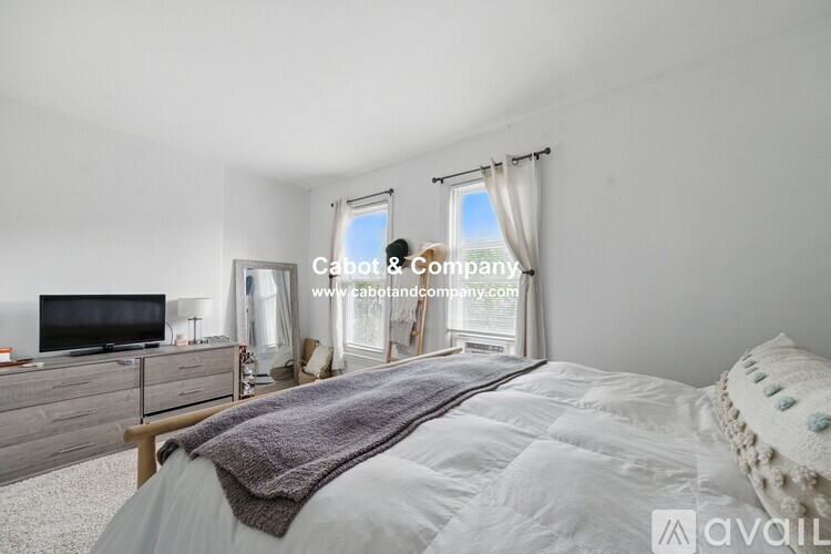 A bedroom with a large bed, a television, and a window with curtains.