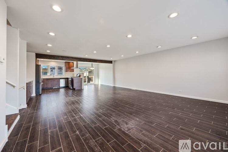 A spacious room with wooden flooring and a staircase on the left side.
