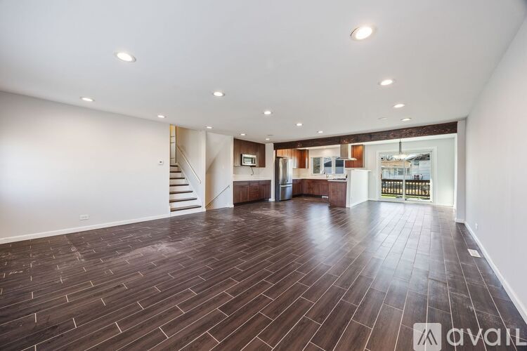 A spacious room with wooden flooring and a staircase in the background.