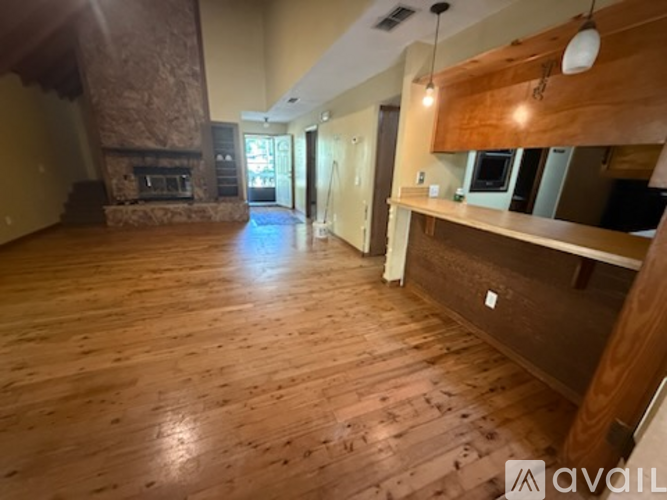 A spacious room with wooden flooring and a stone fireplace.