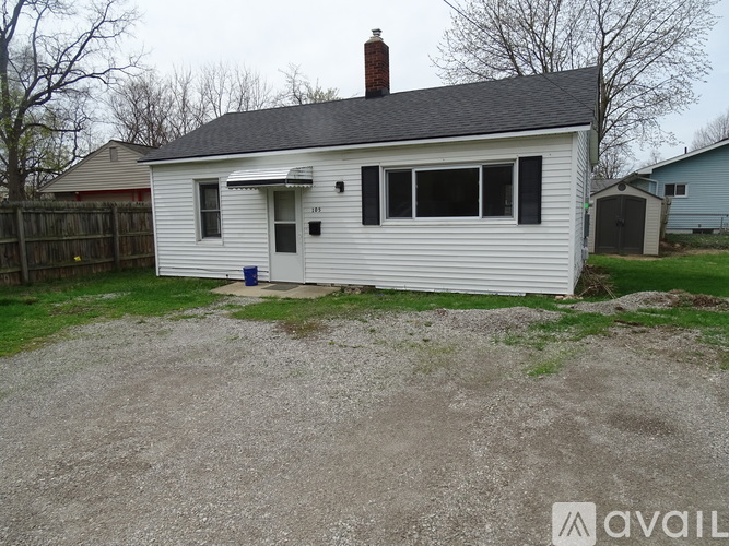 A small white house with a gravel driveway in front.