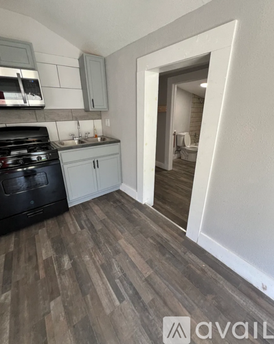 A kitchen with a black stove top oven and wooden flooring.