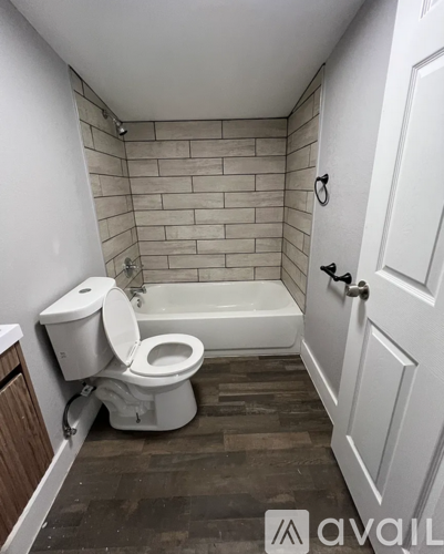 A bathroom with a toilet, tub, and wooden floor.