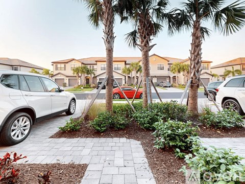 A white car is parked in a driveway next to a red car.