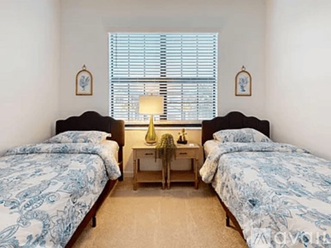 A bedroom with two beds and a nightstand with a lamp.