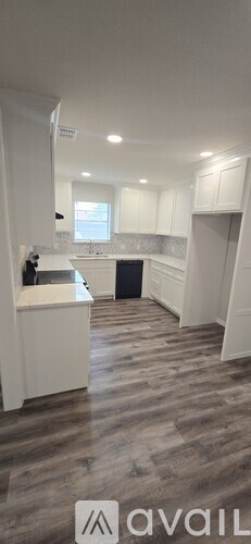 A modern kitchen with white cabinets and a wooden floor.