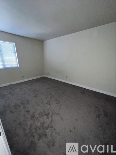 A room with a grey carpet and a window.