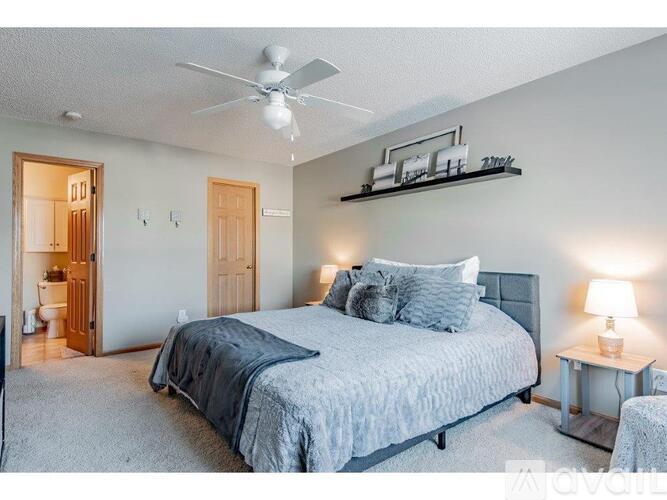 A bedroom with a bed, a ceiling fan, and a nightstand with a lamp.
