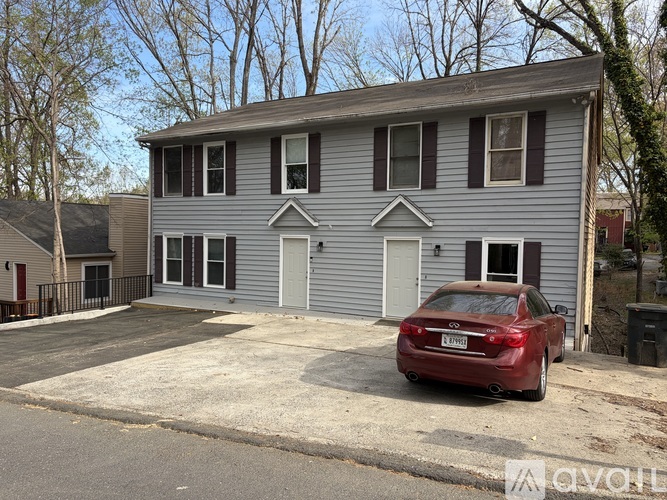 A red car is parked in front of a grey house.