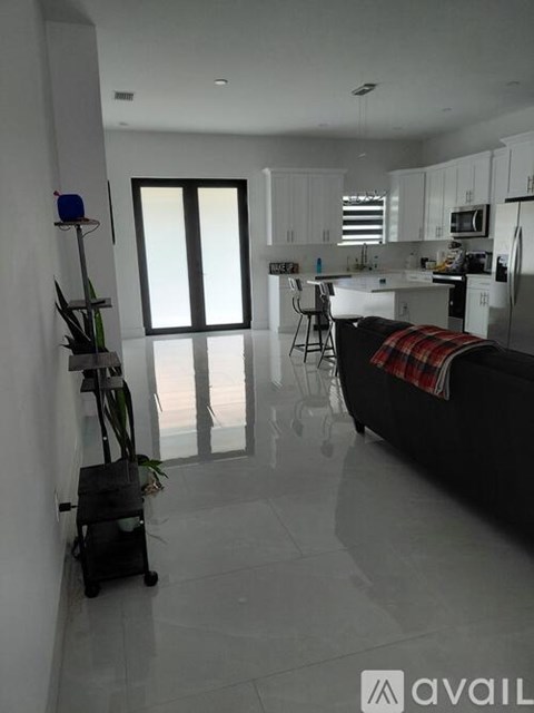 A modern kitchen with white cabinets and a black couch with a plaid throw.