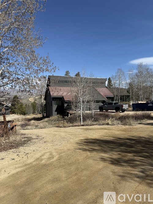 A large, old building with a red roof sits in a field with a dirt road leading up to it.