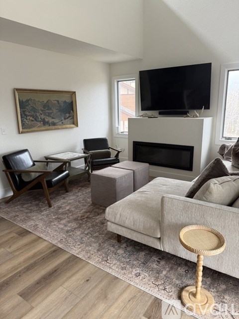 A living room with a grey couch, a black chair, a wooden table, a television, and a painting on the wall.