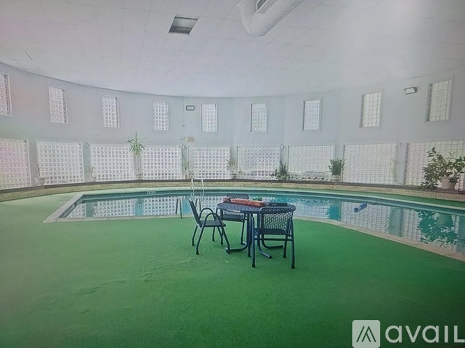 A round table with four chairs is set up on a green floor next to a pool.