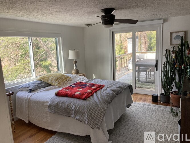 A bedroom with a bed, a ceiling fan, and a view of the backyard through a sliding glass door.