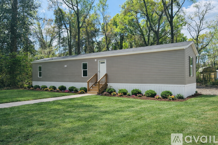 A small house with a grey siding and a brown door is surrounded by a well-kept lawn and trees.