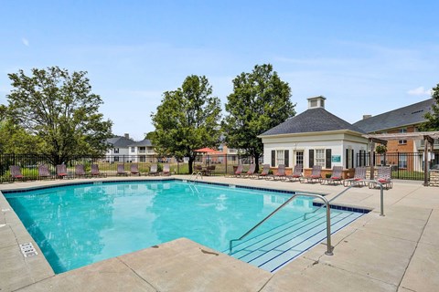 A swimming pool surrounded by a concrete patio and a small building with a black roof.