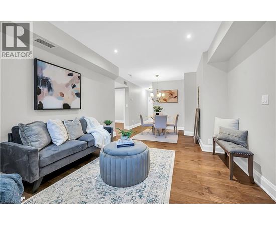 A living room with a grey couch, a blue ottoman, and a painting on the wall.