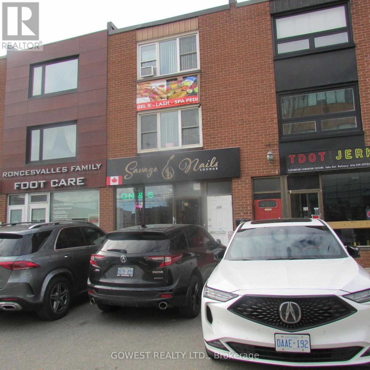A white car is parked in front of a building with a sign that says "Savage & Nails.".