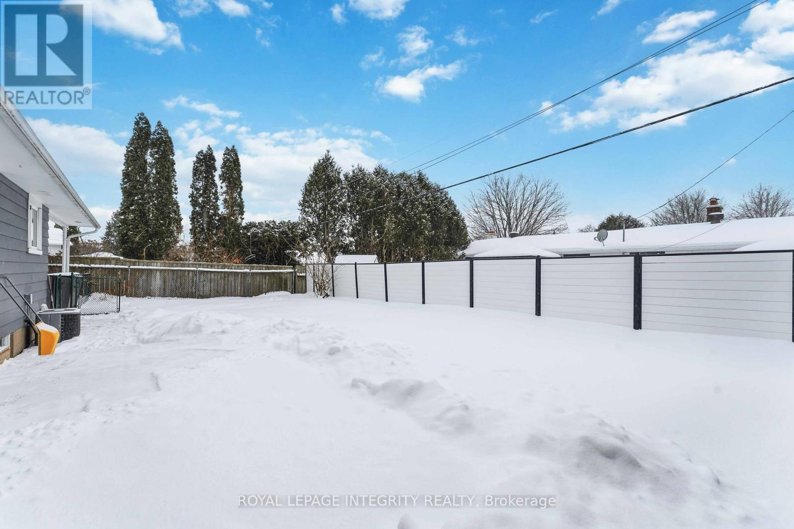 A snow-covered yard with a fence and trees in the background.