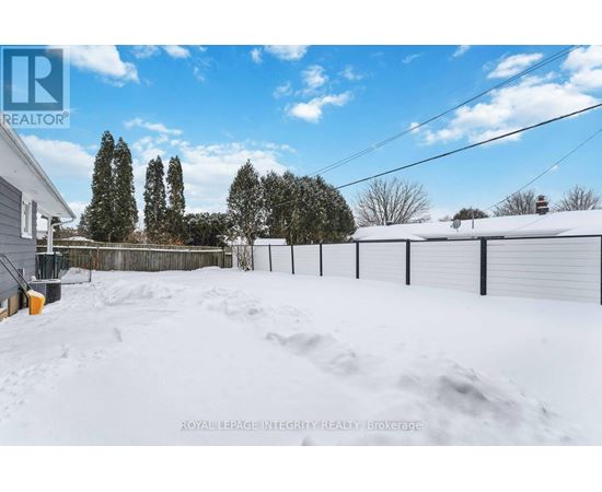 A snow-covered yard with a fence and trees in the background.