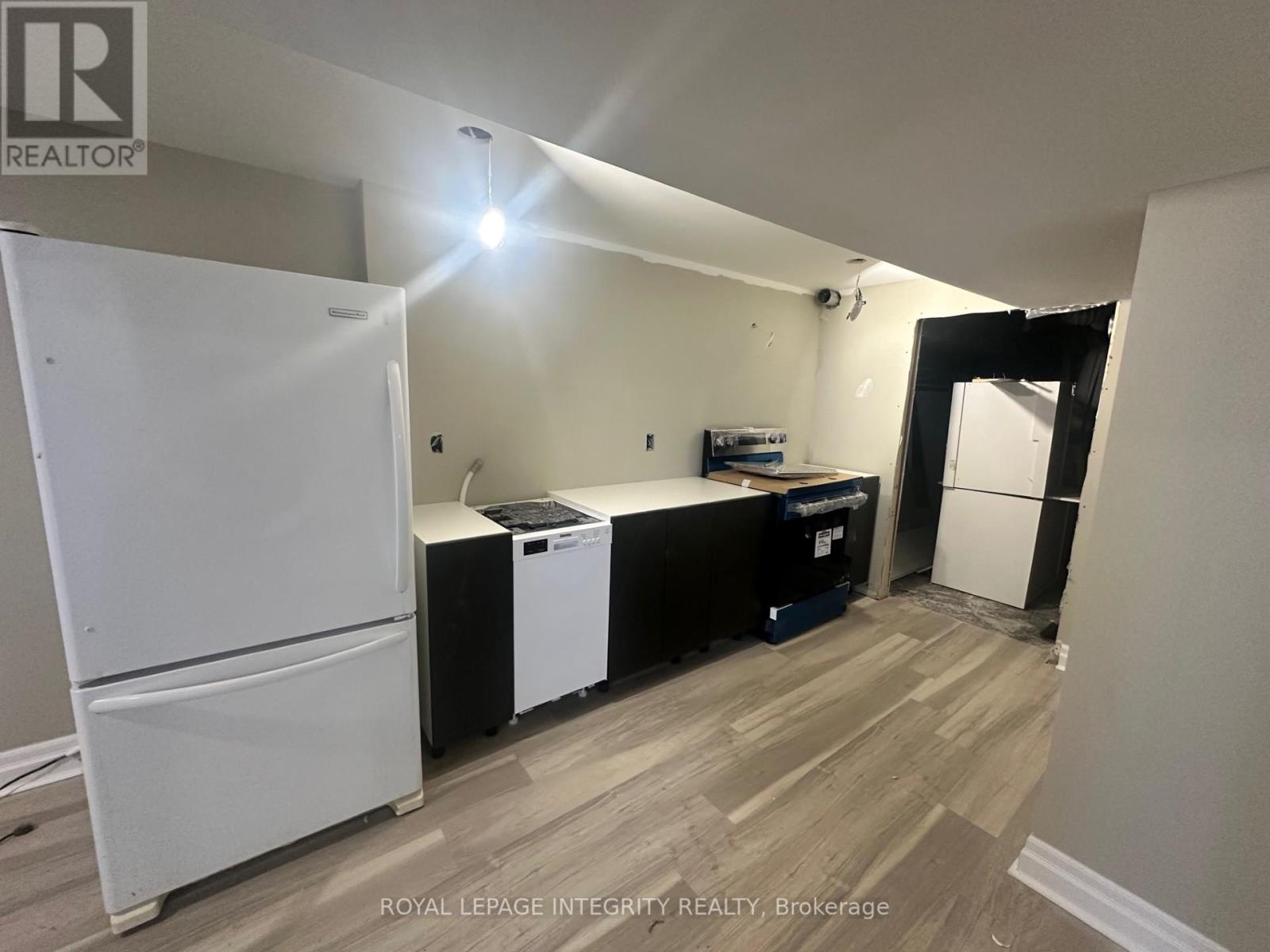 A white refrigerator stands in a kitchen with a black dishwasher and a white washing machine.