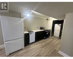 A white refrigerator stands in a kitchen with a black dishwasher and a white washing machine.