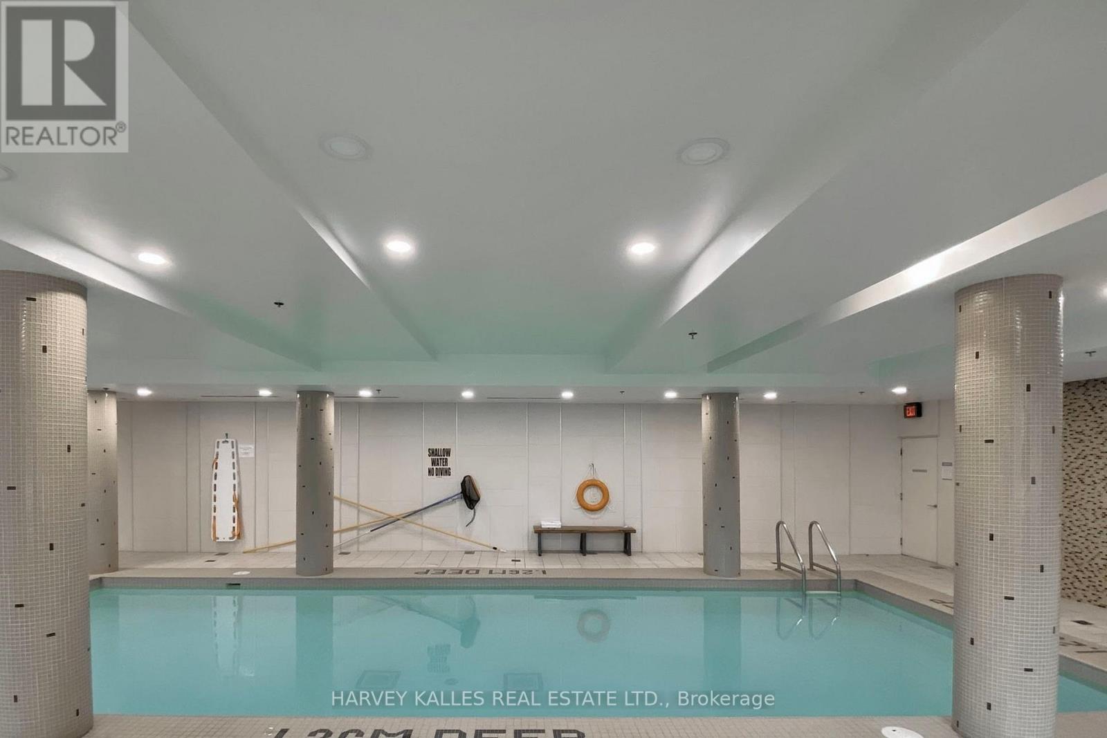 A swimming pool inside a building with a sign that says Harvey Kalles Real Estate Ltd.