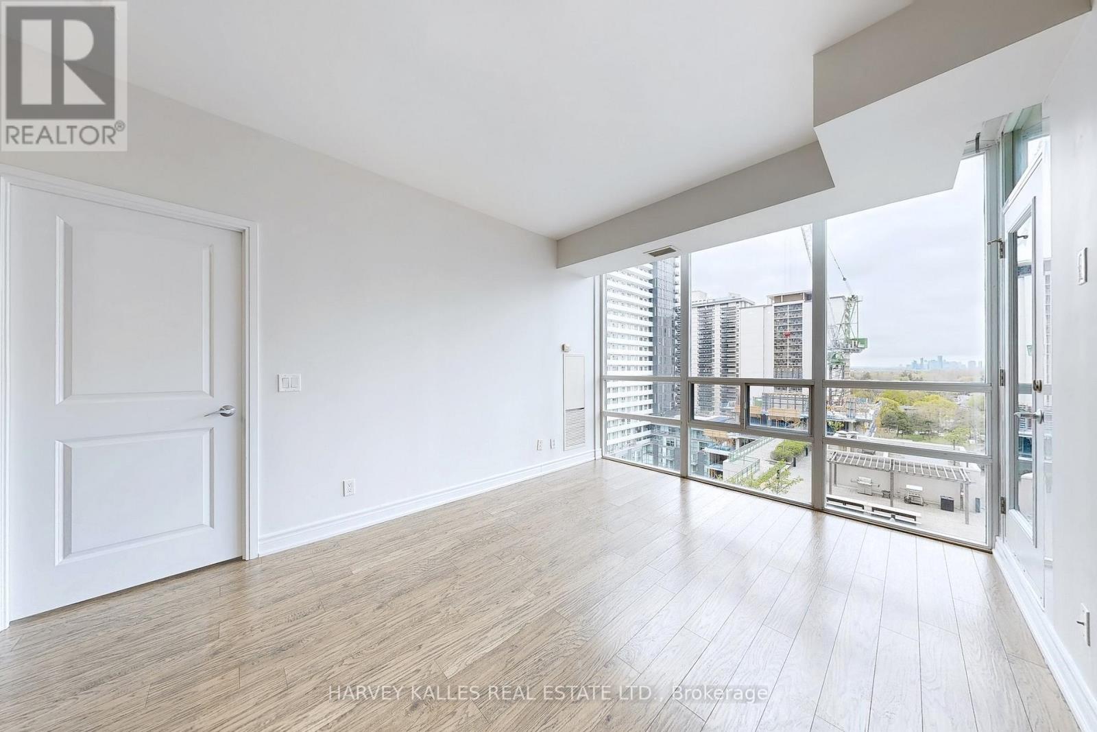 A spacious room with wooden flooring and a view of the city through the windows.