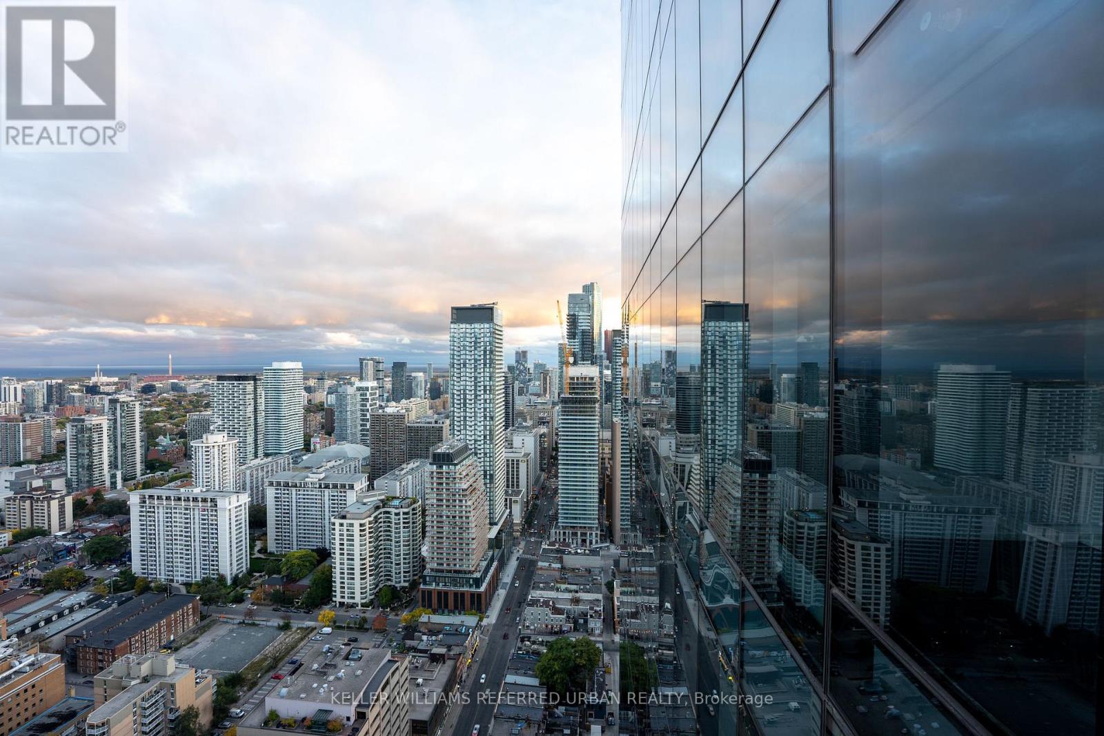 A cityscape with a glass building in the foreground and a cloudy sky above.