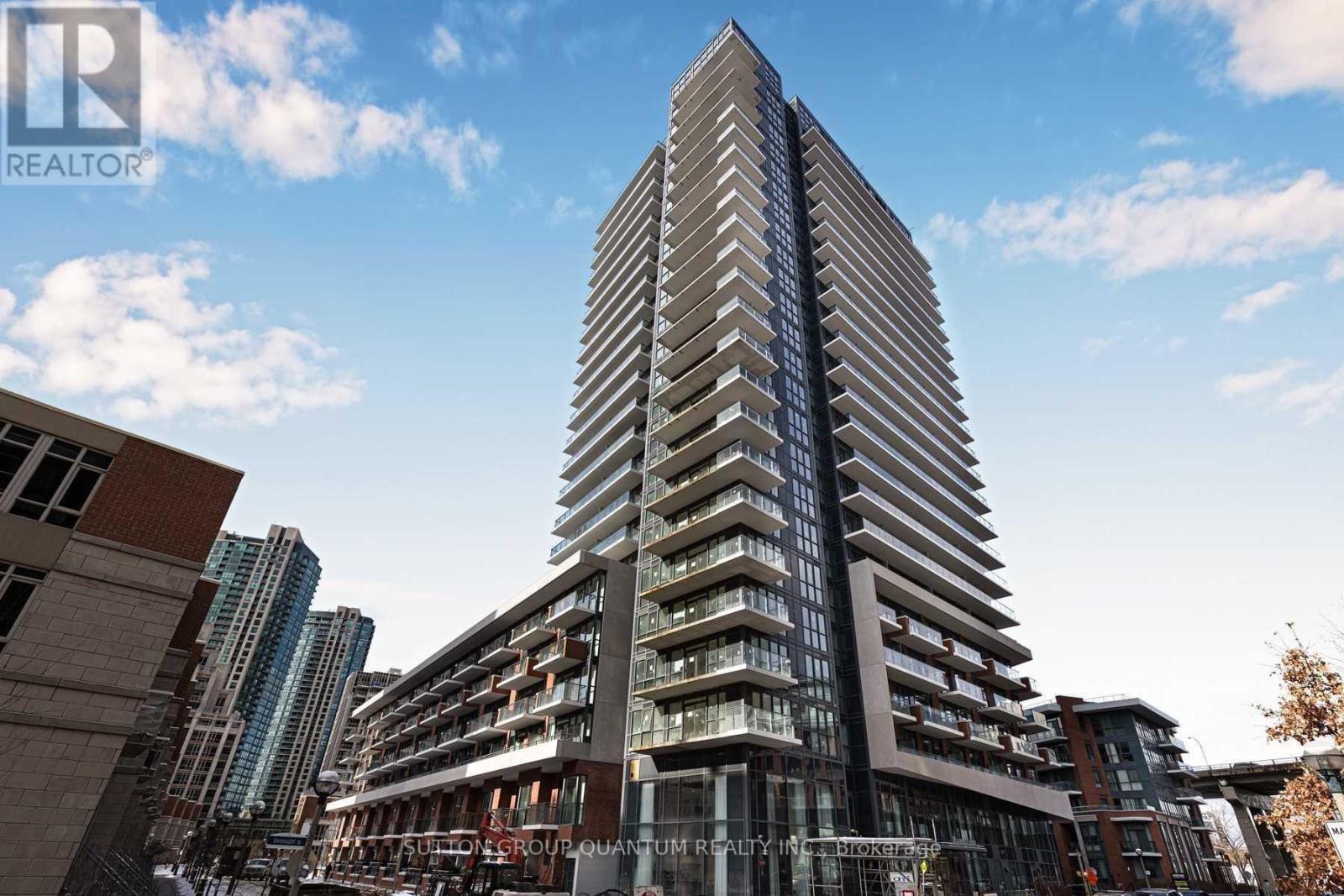 A tall building with a glass facade stands in front of other buildings.