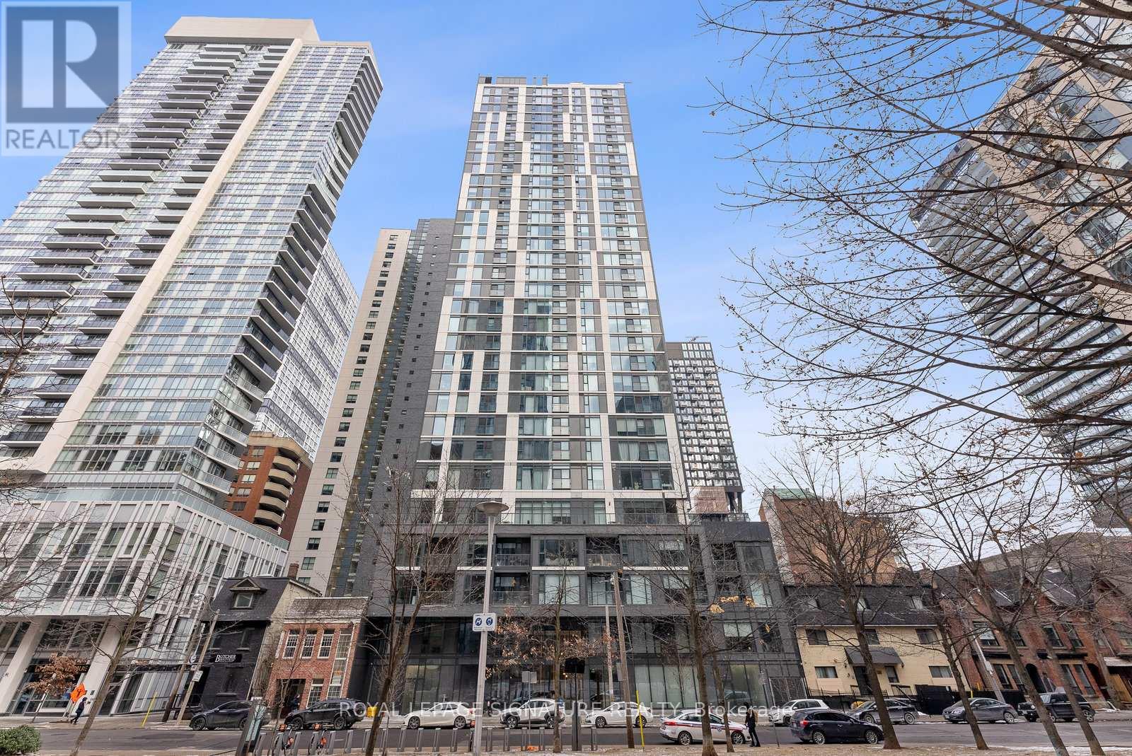 A tall building with a glass facade stands in front of other buildings.