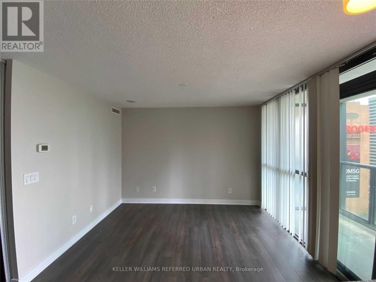 A spacious room with a large window and wooden flooring.