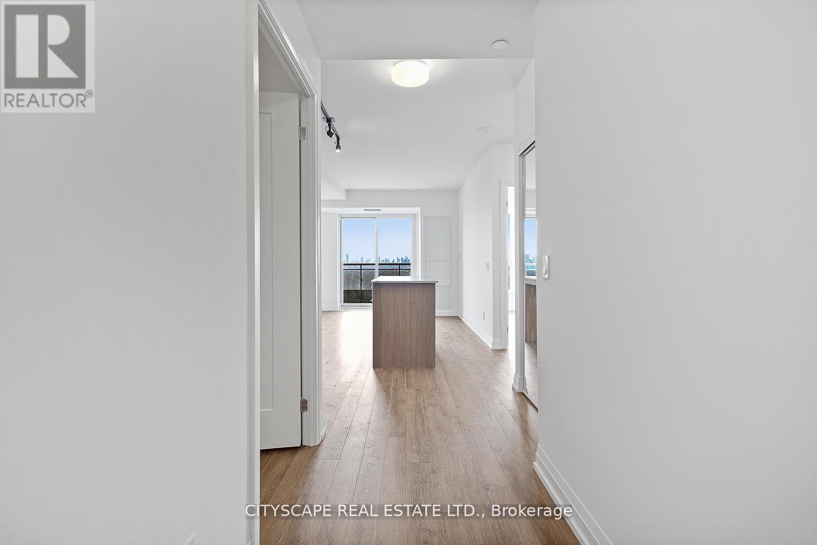 A real estate listing image of a white room with a wooden floor and a large window.