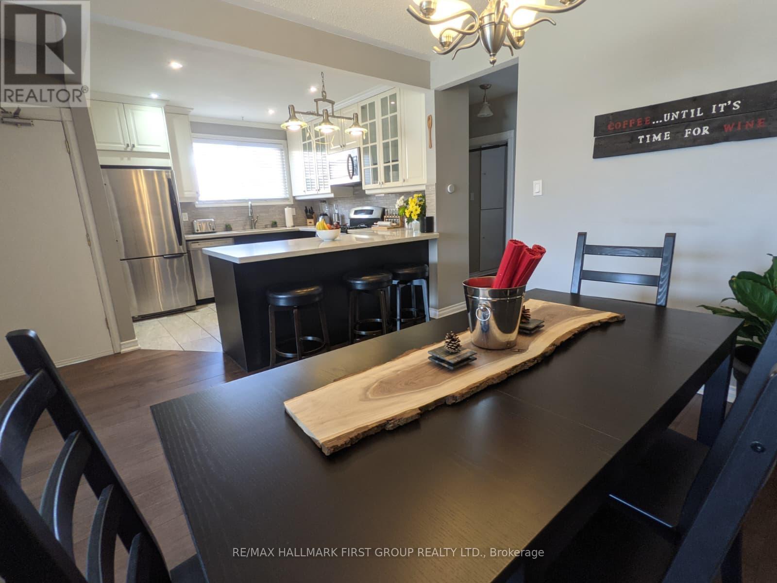 A kitchen with a wooden table and chairs in the foreground and a framed sign on the wall that says "Drink until it's time for wine.".