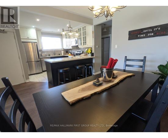 A kitchen with a wooden table and chairs in the foreground and a framed sign on the wall that says "Drink until it's time for wine.".