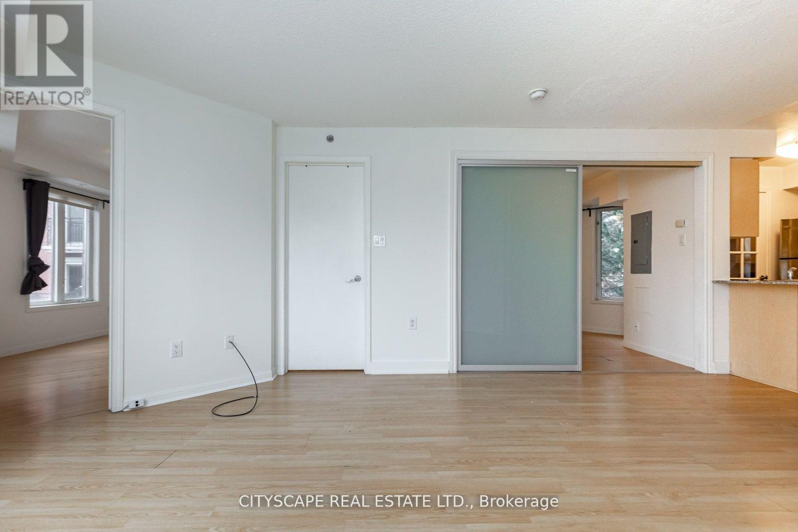 A real estate listing image of a white room with wood floors and a single door.