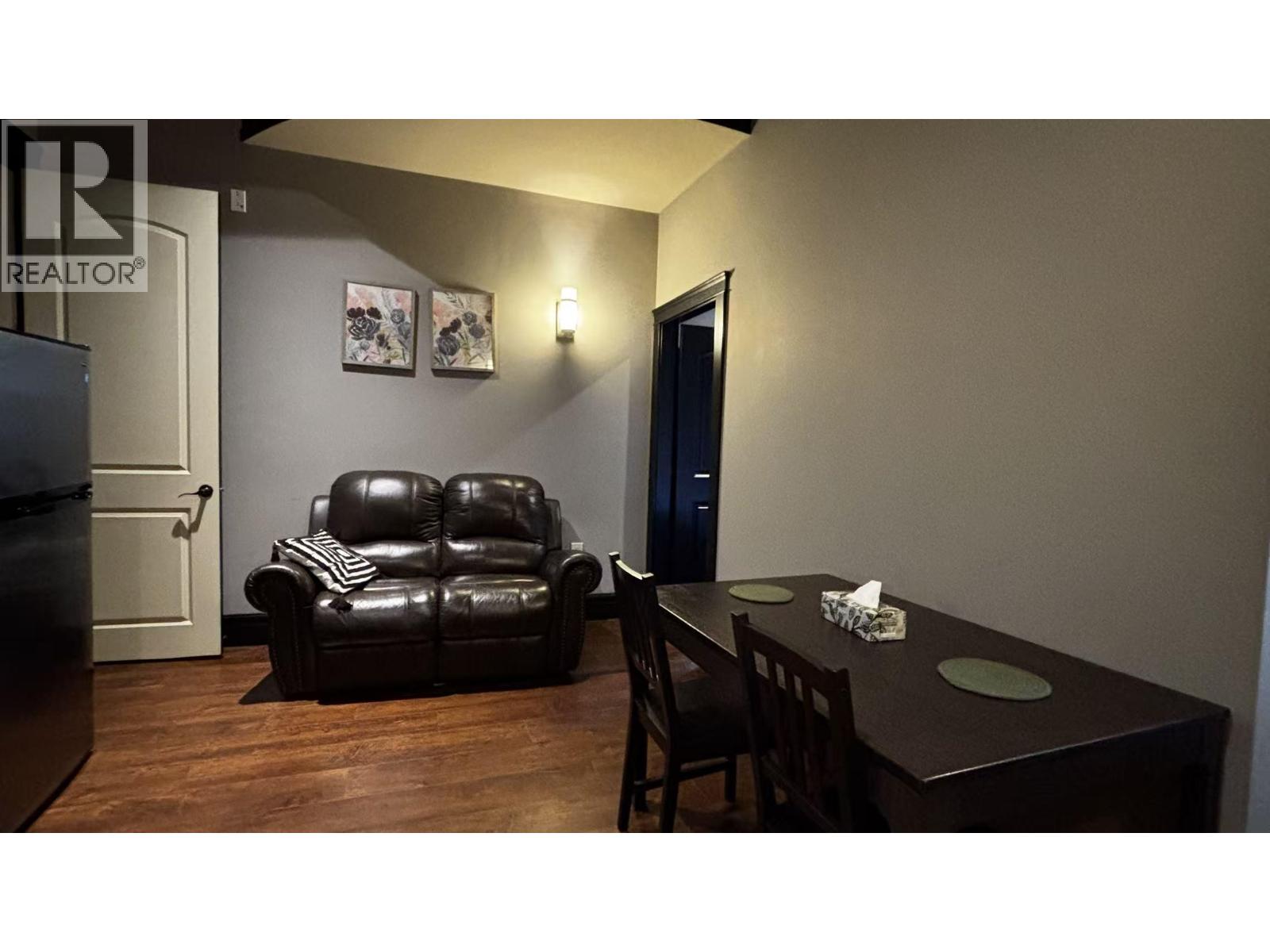 A black leather sofa sits in a living room with a wooden table and chairs.