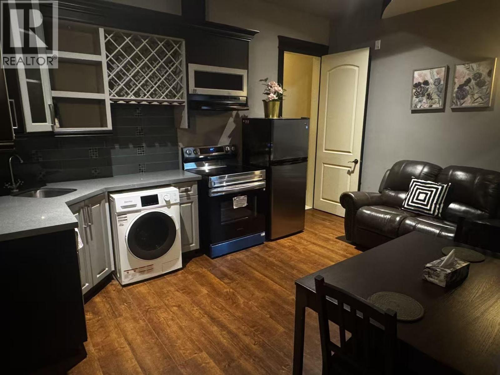 A kitchen with a black fridge and a black couch.