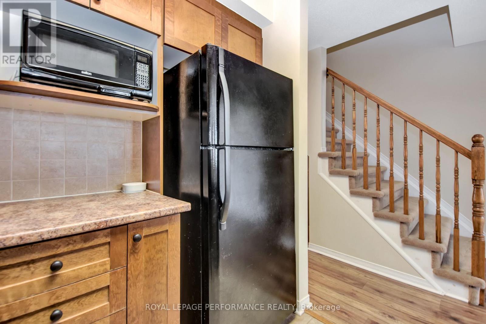 A black fridge in a kitchen with wooden cabinets and a staircase in the background.