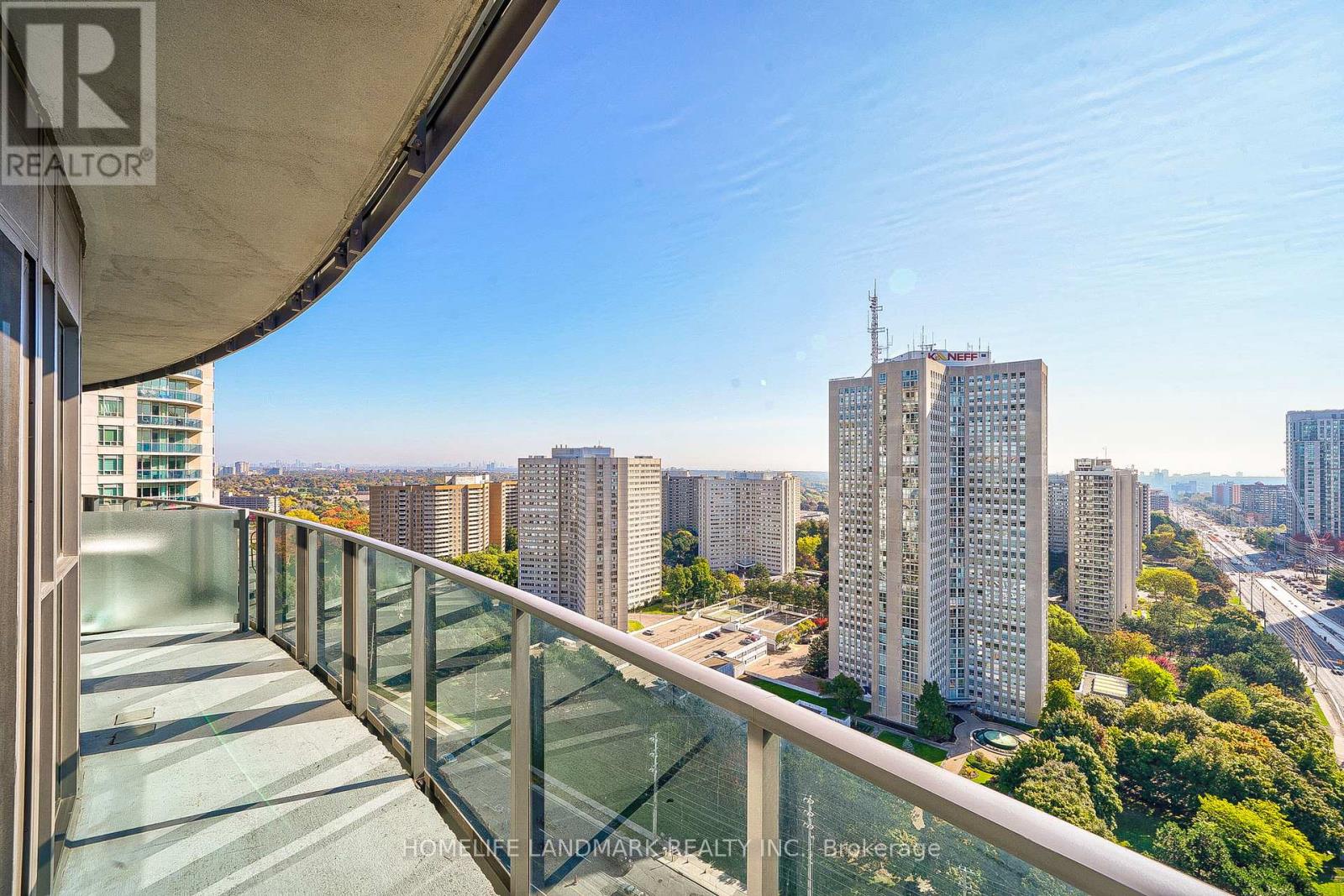 A balcony with a glass railing overlooks a cityscape with tall buildings.