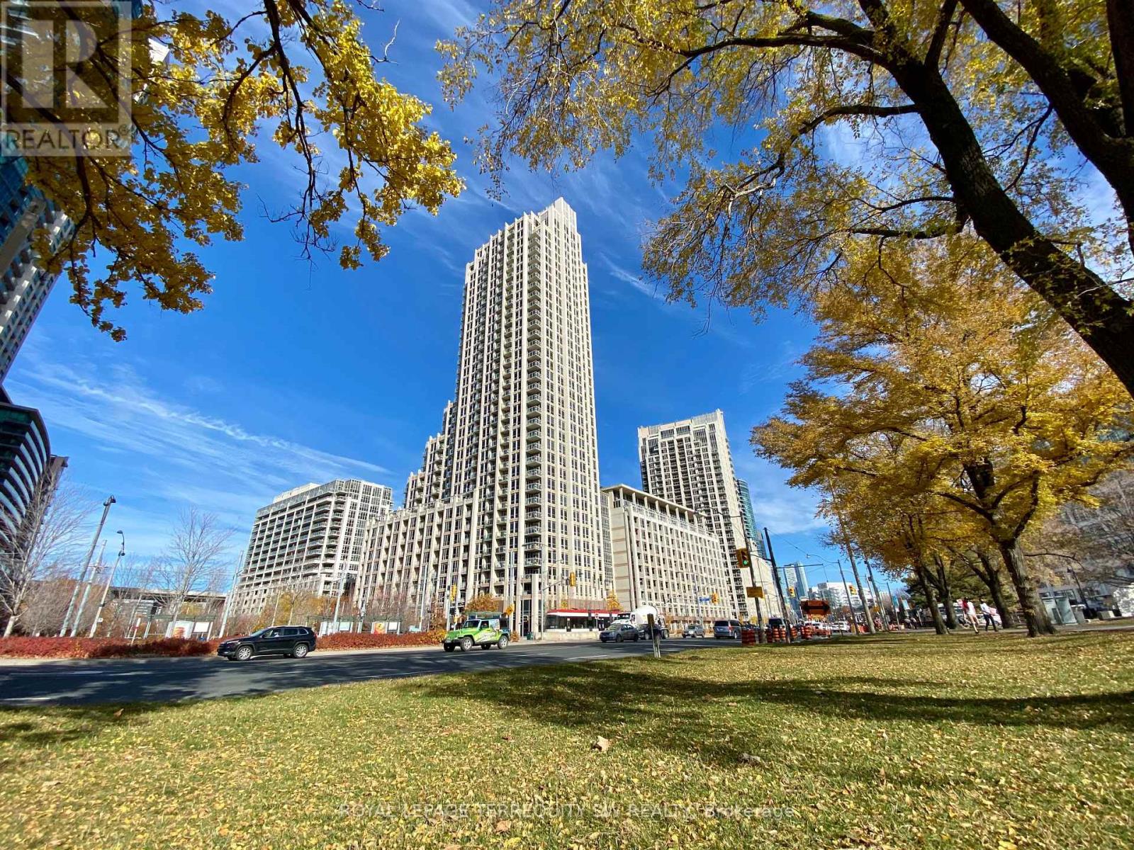 A tall building stands in the middle of a park with trees showing autumn leaves.